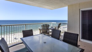 Ein Balkon mit Glastisch und Korbstühlen, der auf einen Strand mit dem Meer und einem klaren Himmel blickt.