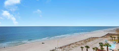 A beach resort with a sandy beach, a pool area, and a clear view of the ocean.