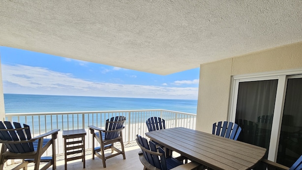 Een balkon met uitzicht op de oceaan, houten meubels en een glazen deur.