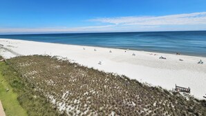Een strand met wit zand, helderblauw water en een gazon met een hek.