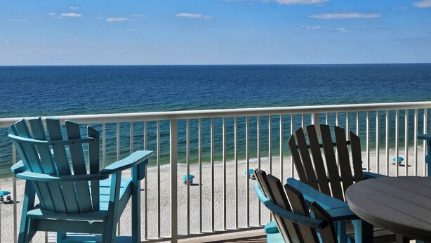 A balcony with a view of the ocean, featuring two blue Adirondack chairs and a small table. - Sandy Key 731: 3 BR/2 BA Perdido Key Beachfront Condo, On-Site Rental Office, Sleeps 8 (Pensacola)