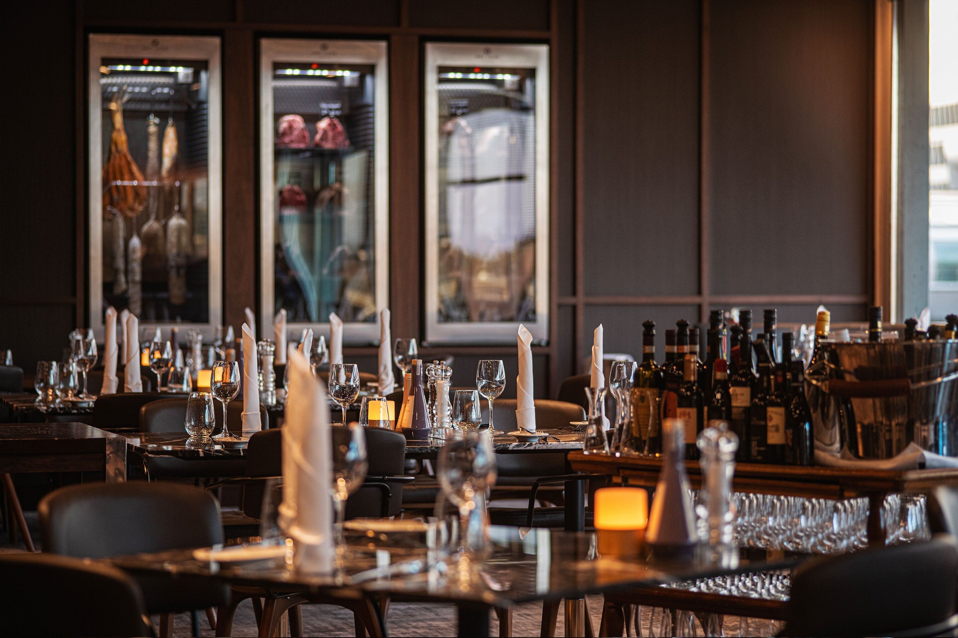 A restaurant with tables set for dining, featuring candles, wine glasses, and bottles.