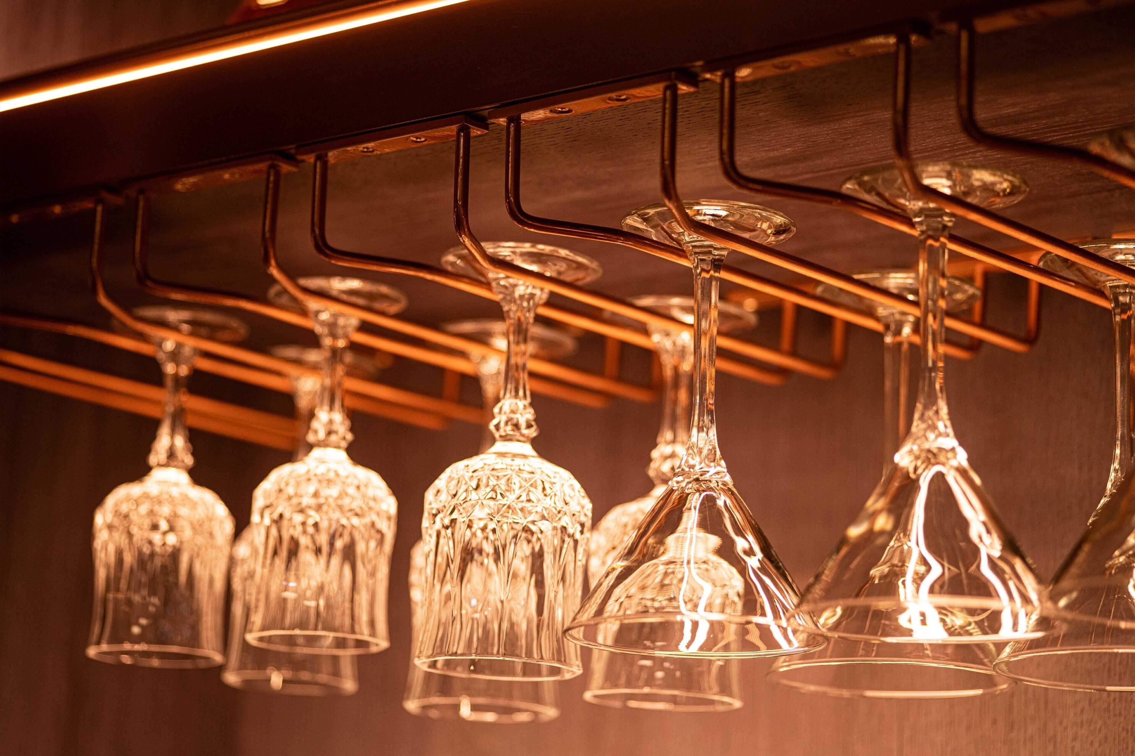 A row of hanging wine glasses with a warm light source above them.