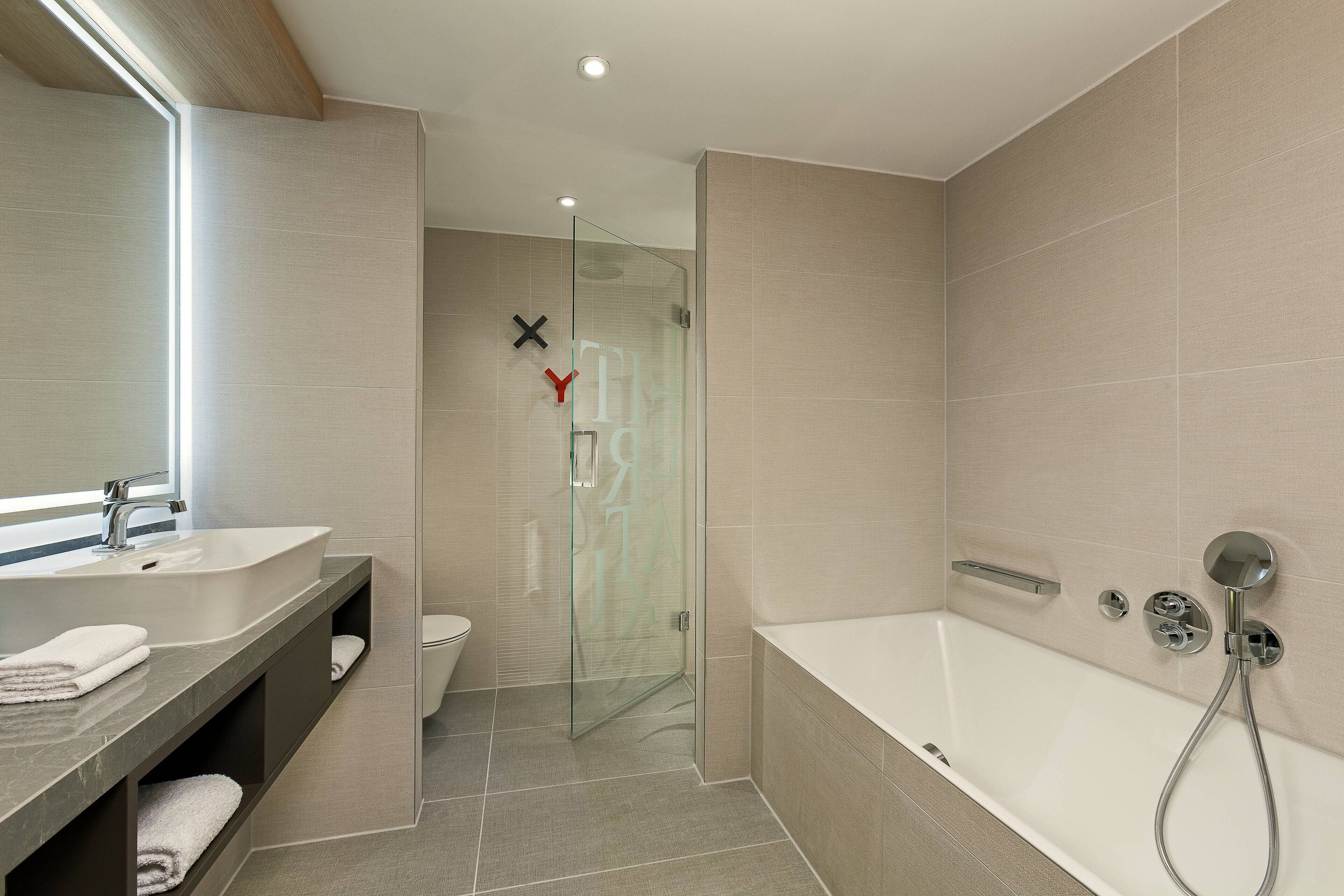 A modern bathroom with a glass shower enclosure, a bathtub, and a vanity with a sink and towel rack.
