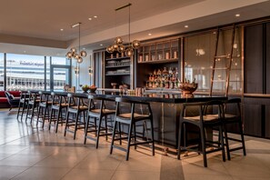A modern bar area with a long counter, bar stools, and a variety of bottles and glasses. - Frankfurt Airport Marriott Hotel (Frankfurt)