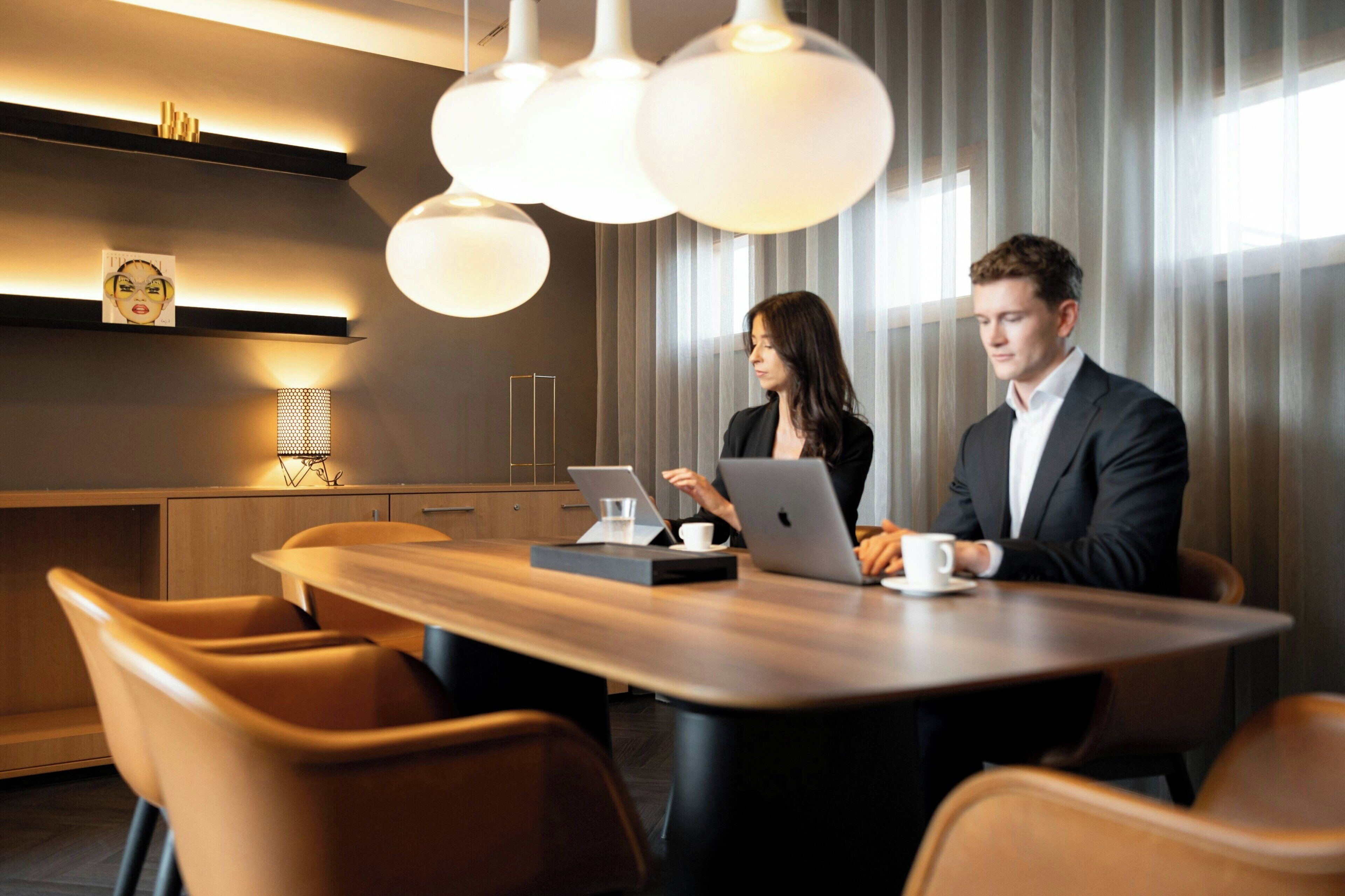Una sala de conferencias moderna con una mesa de madera, sillas de cuero e iluminación colgante.