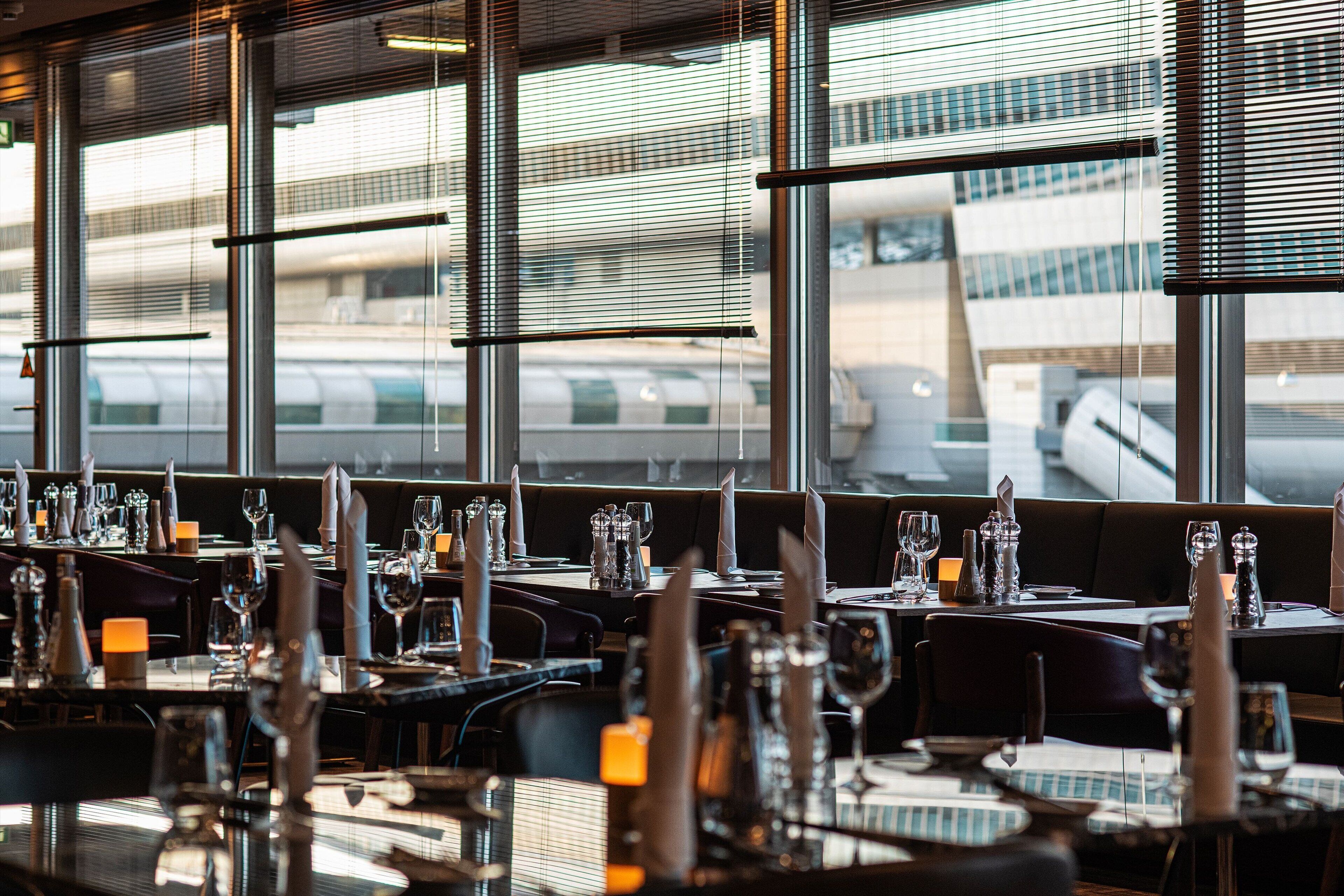 A restaurant with tables set for dining, large windows, and a view of an airport.