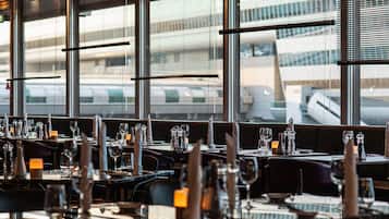 A restaurant with tables set for dining, large windows, and a view of an airport.