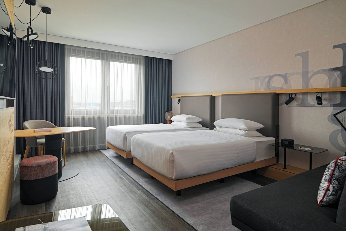A modern hotel room with two beds, a sofa, a dining table, and a small seating area.