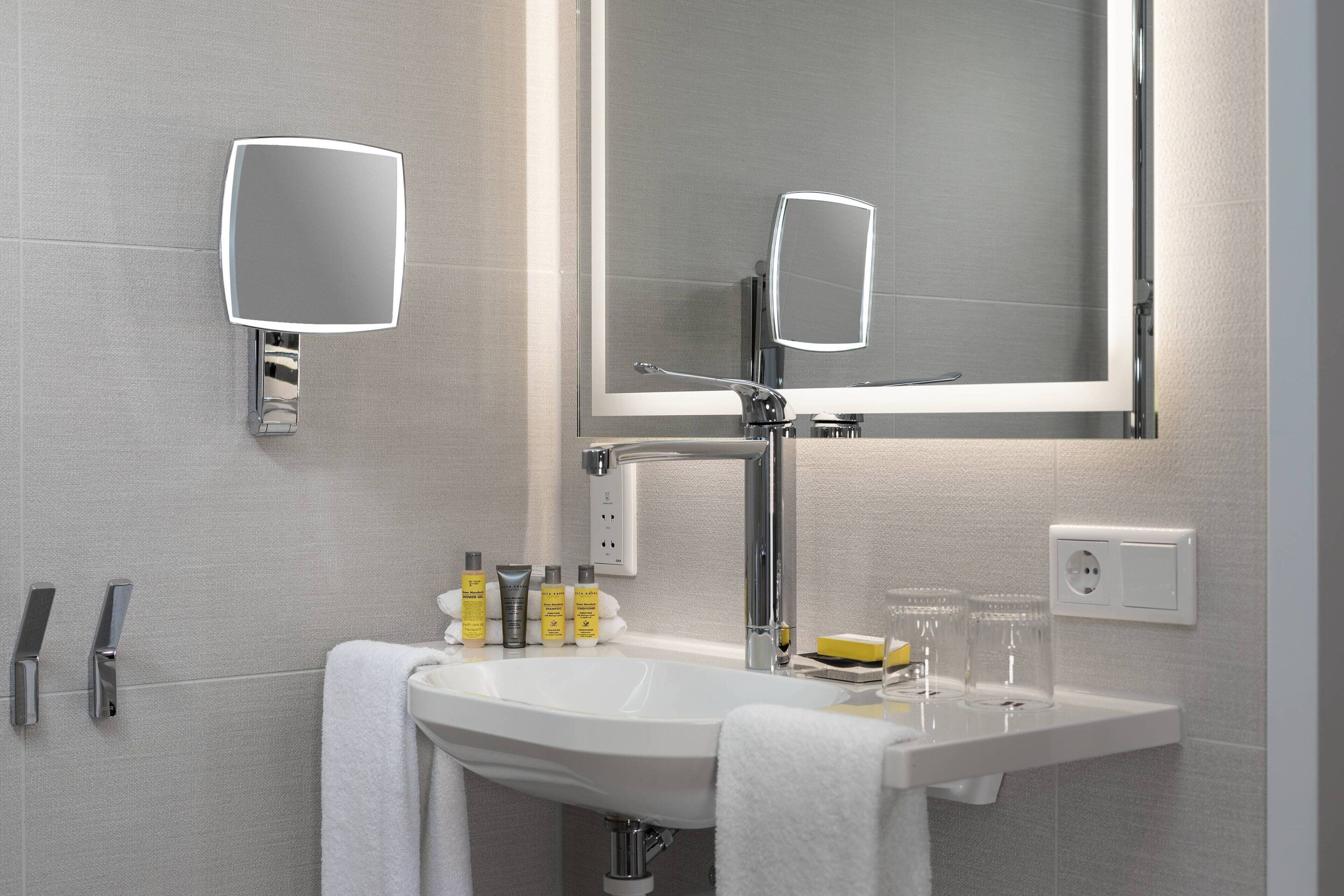 A modern bathroom with a white sink, two wall-mounted mirrors, and a towel rack.