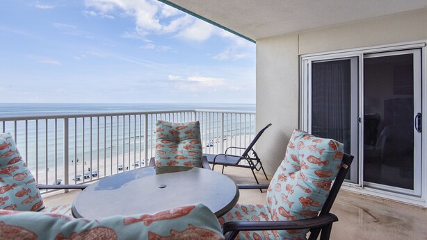 Un balcón con vista a la playa, una mesa redonda y dos sillas con cojines estampados.