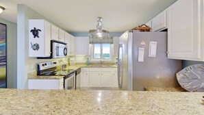 Una cocina con armarios blancos, un refrigerador de acero inoxidable, un microondas y una encimera de granito.