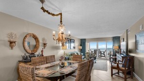 Un salón espacioso con una gran mesa de comedor, muebles de mimbre y una araña.