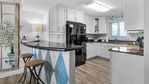 Una cocina moderna con armarios blancos, un refrigerador negro, encimera de mármol y una zona de bar con taburetes.