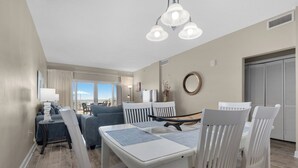 A modern living room with a dining area, featuring a sofa, chairs, a table, and a view of the outdoors. - Sandy Key 126: 2 BR/2 BA Beachfront Condo, Perdido Key, FL. On-Site Rental Office, Sleeps 6 (Pensacola)