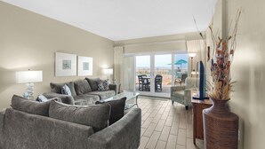 A modern living room with a sofa set, a glass coffee table, and a view of the outdoor patio area. - Sandy Key 126: 2 BR/2 BA Beachfront Condo, Perdido Key, FL. On-Site Rental Office, Sleeps 6 (Pensacola)