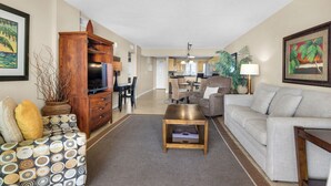 A spacious living room with a sofa, coffee table, and a TV stand. There is a dining area with a table and chairs in the background. - Sandy Key 416:  2 BR / 2BA Gulf Front Condo in Perdido Key, FL.  Sleeps 6 (Perdido Key)