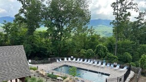 Une piscine rectangulaire entourée de chaises longues, elle-même bordée d’une terrasse en pierre et d’une clôture en bois.