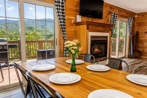 A dining area with a wooden table set for four, a fireplace, and a view of the outdoors.