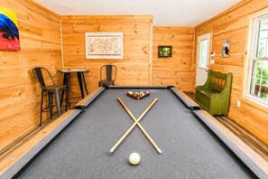 Een pooltafel met twee stokken en een witte poolbal, omringd door houten wanden en een lijst met een kaart.