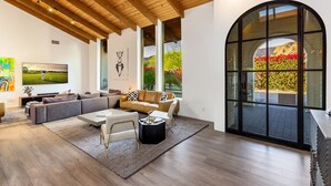 A modern living room with a large arched window, a flat-screen TV, and a cozy seating area. - Luxury Camelback Mountain Views, Theater, Sauna, Heated Pool, Spa (Phoenix)