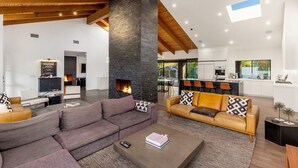 A spacious living area with a fireplace, modern furniture, and a kitchen in the background. - Luxury Camelback Mountain Views, Theater, Sauna, Heated Pool, Spa (Phoenix)