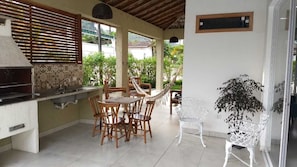 A kitchen with a grill, dining table with chairs, and a potted plant. - Wonderful house with pool in the gated community Ubatuba Country (Ubatuba)
