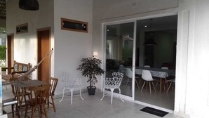 Un espace patio aménagé avec une table et des chaises en bois, une plante en pot et une porte-fenêtre coulissante donnant sur une salle à manger intérieure.