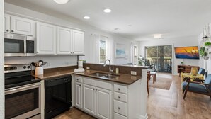 A modern kitchen with white cabinets, stainless steel appliances, and a large island with a sink. - Perfect Year-Round! 2nd floor golf course condo, pool & hot tub, close to beach (Pawleys Island)