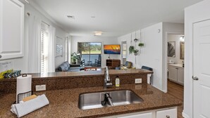 A kitchen with granite countertops, a stainless steel sink, and a dining area with a view of the outdoors. - Perfect Year-Round! 2nd floor golf course condo, pool & hot tub, close to beach (Pawleys Island)
