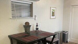 Ein Essbereich mit einem für zwei Personen gedecktem Tisch, einem Mülleimer und einem Fenster mit Jalousien.