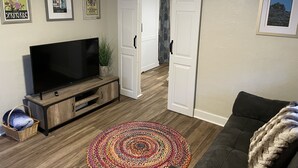 Ein Wohnzimmer mit Fernseher, einer Couch, einem farbenfrohen Teppich und einer Schiebetür.
