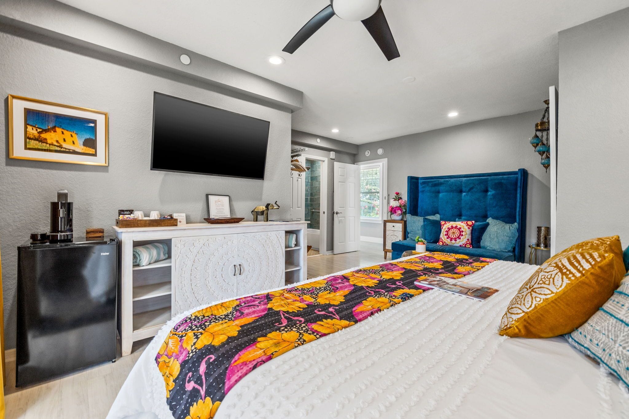 Une chambre moderne équipée d’un lit, d’une tête de lit bleue, d’un téléviseur à écran plat, d’un mini-bar et d’une porte donnant accès à une salle de bain.