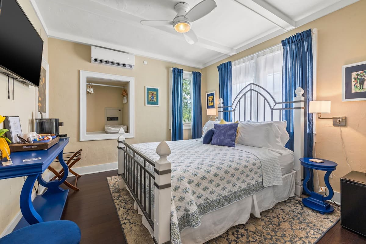 A bedroom with a bed, a desk, a chair, a ceiling fan, and a window with curtains.