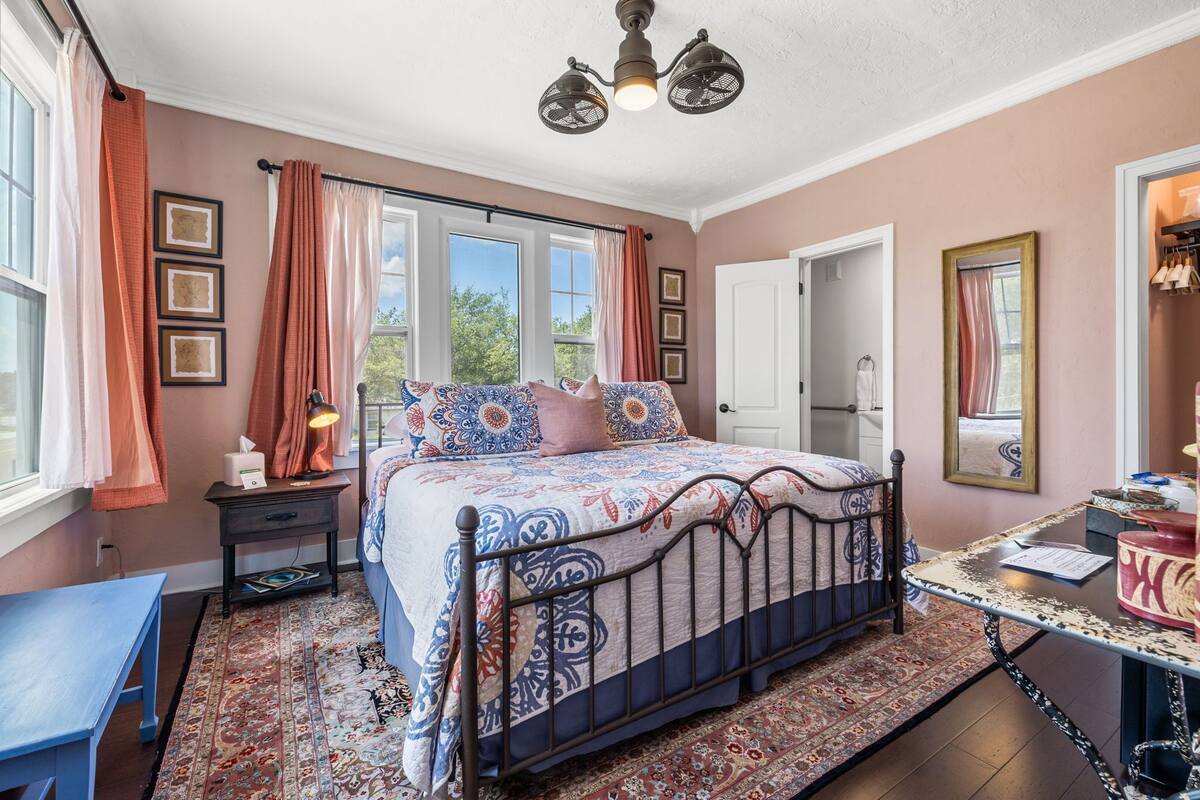 A bedroom with a bed, bedside table, lamp, and a view of the outdoors.