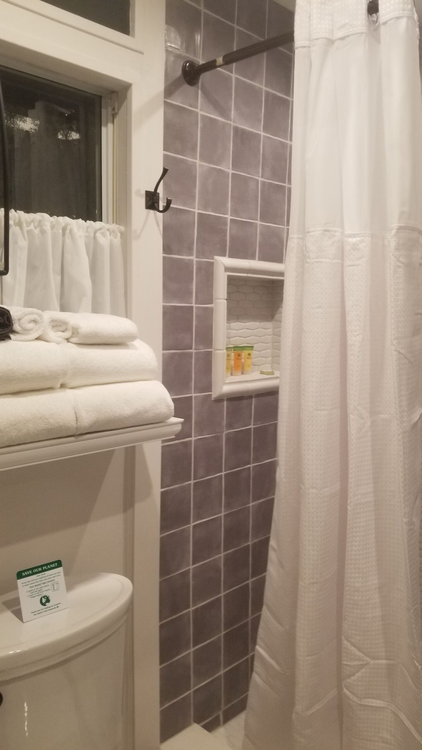 A bathroom with a shower curtain, a towel rack with folded towels, a toilet, and a shelf with toiletries.