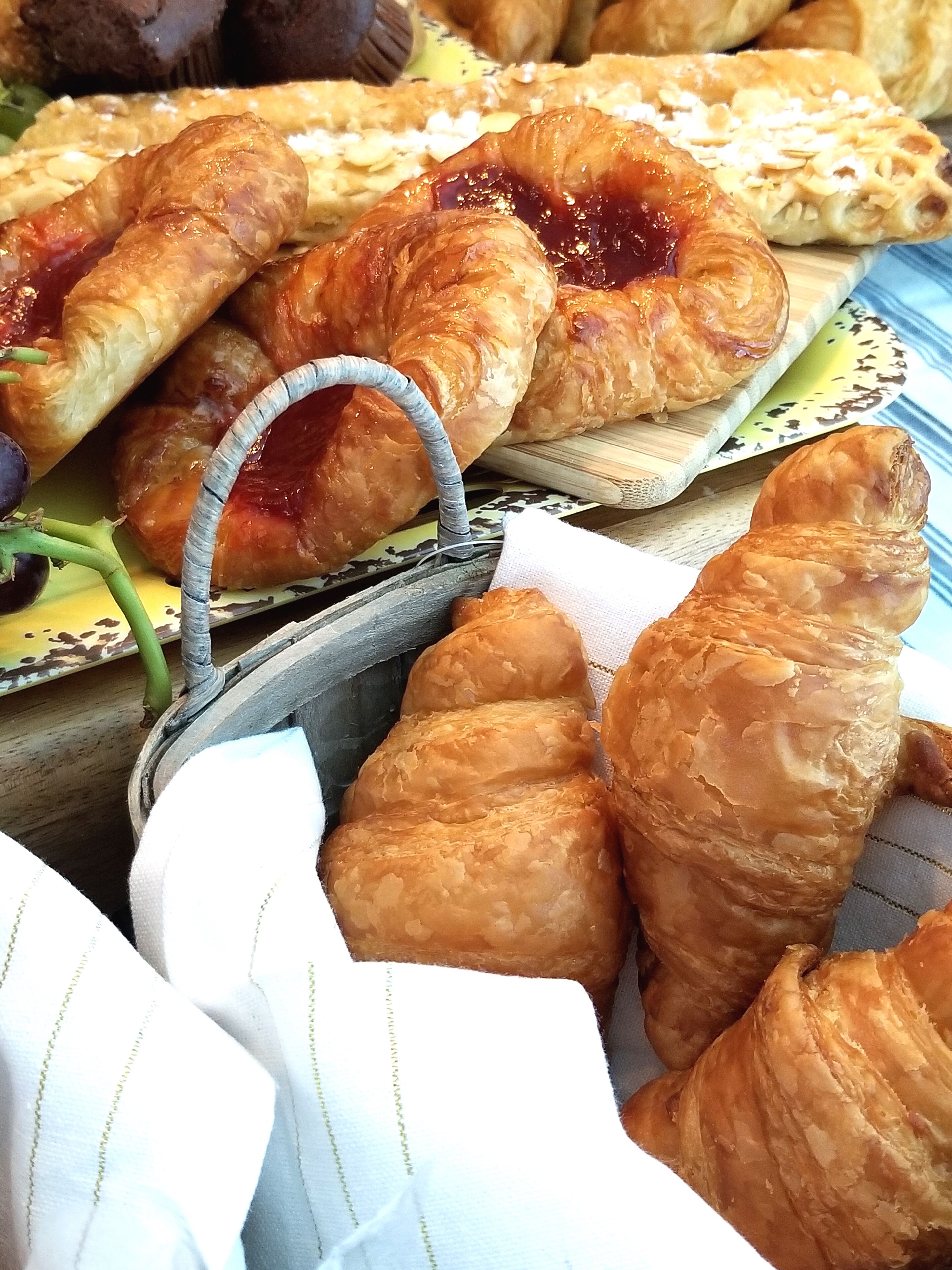 Erilaisia leivonnaisia, kuten croissantteja ja leivonnaisia, joissa on kahva, esillä puisen tarjottimen päällä.