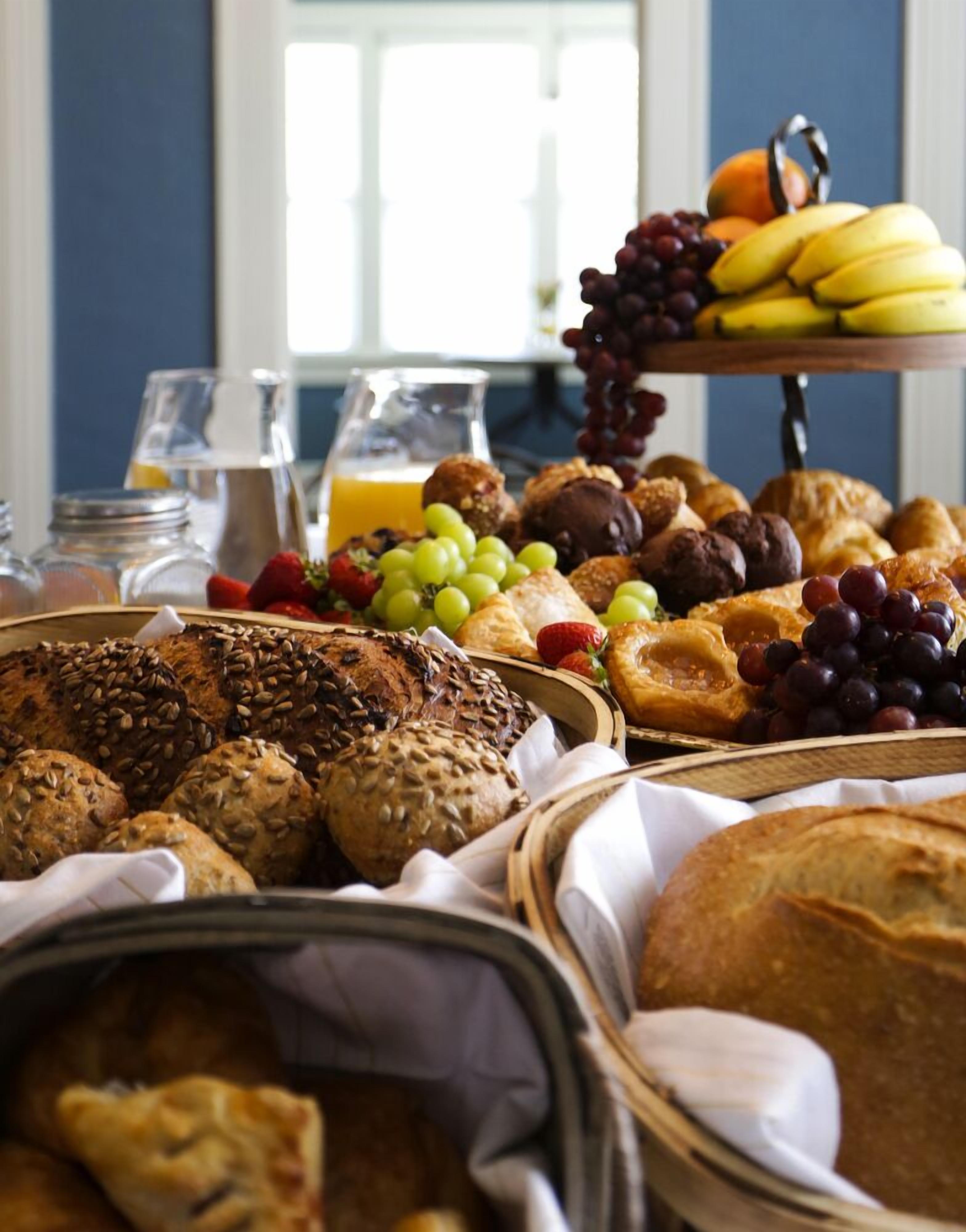 A breakfast buffet with various breads, pastries, fruits, and a glass of orange juice.