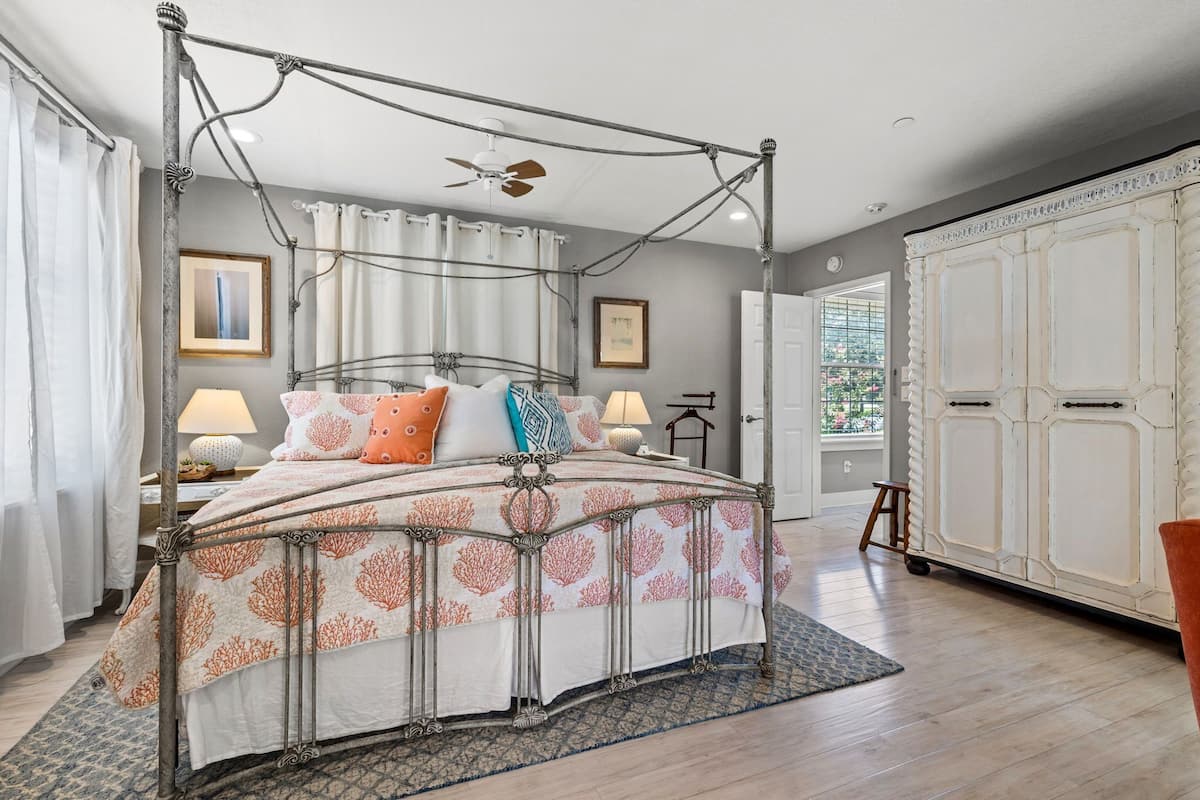 A four-poster bed with a patterned bedspread, two bedside lamps, and a ceiling fan.