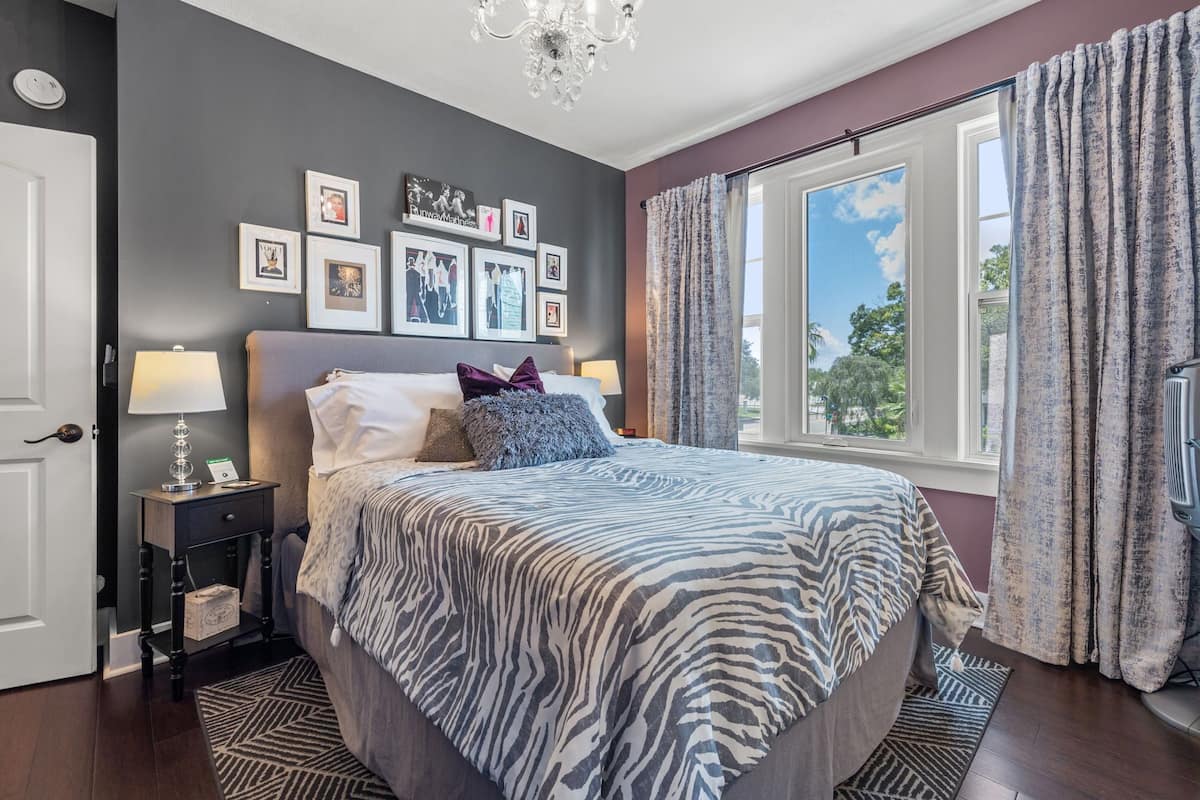 A bedroom with a zebra-patterned bedspread, a chandelier, framed pictures on the wall, and a window with curtains.