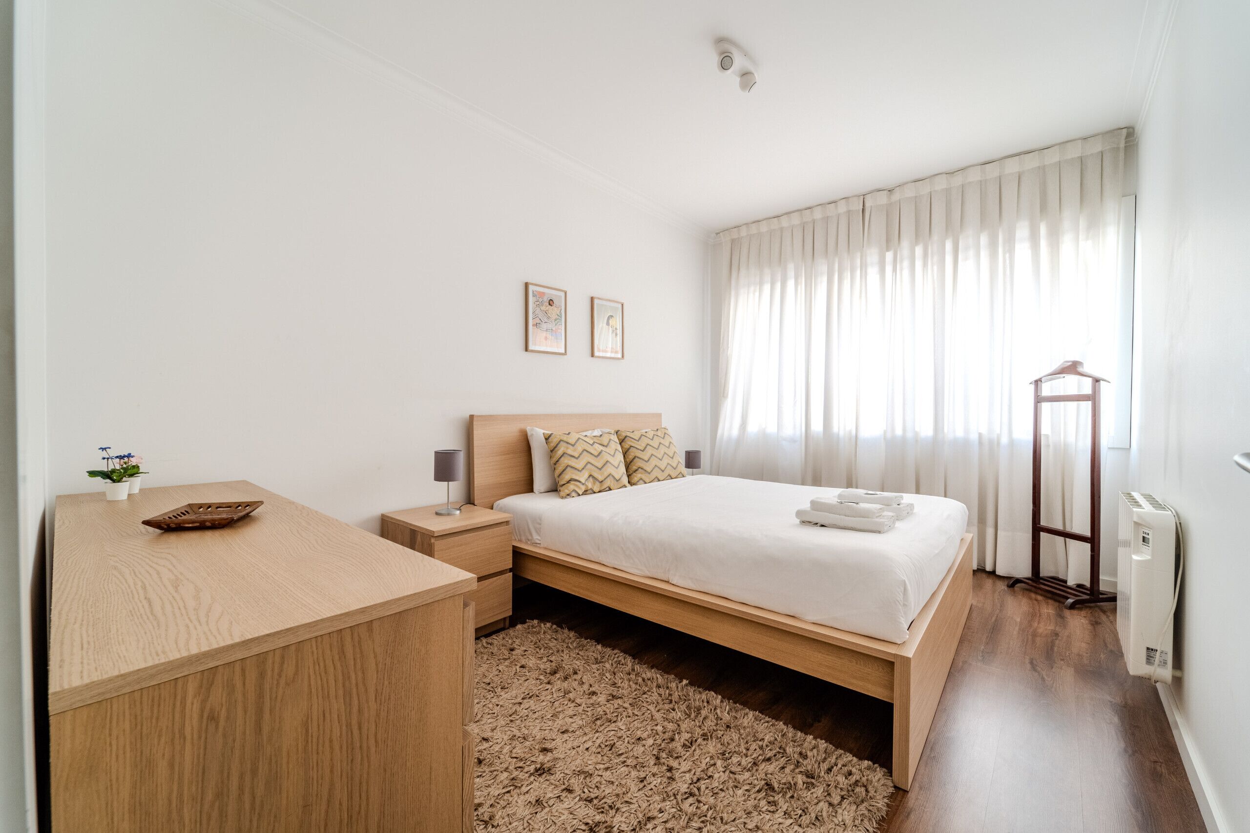 Un dormitorio con cama de madera, una mesita de noche, un escritorio pequeño y un radiador.