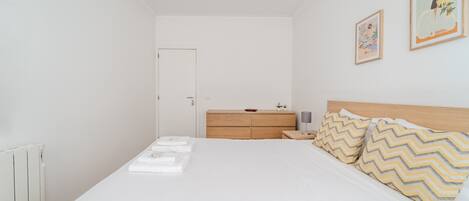 Un dormitorio con una cama, un aparador de madera, una mesita de noche y dos cuadros enmarcados en la pared.