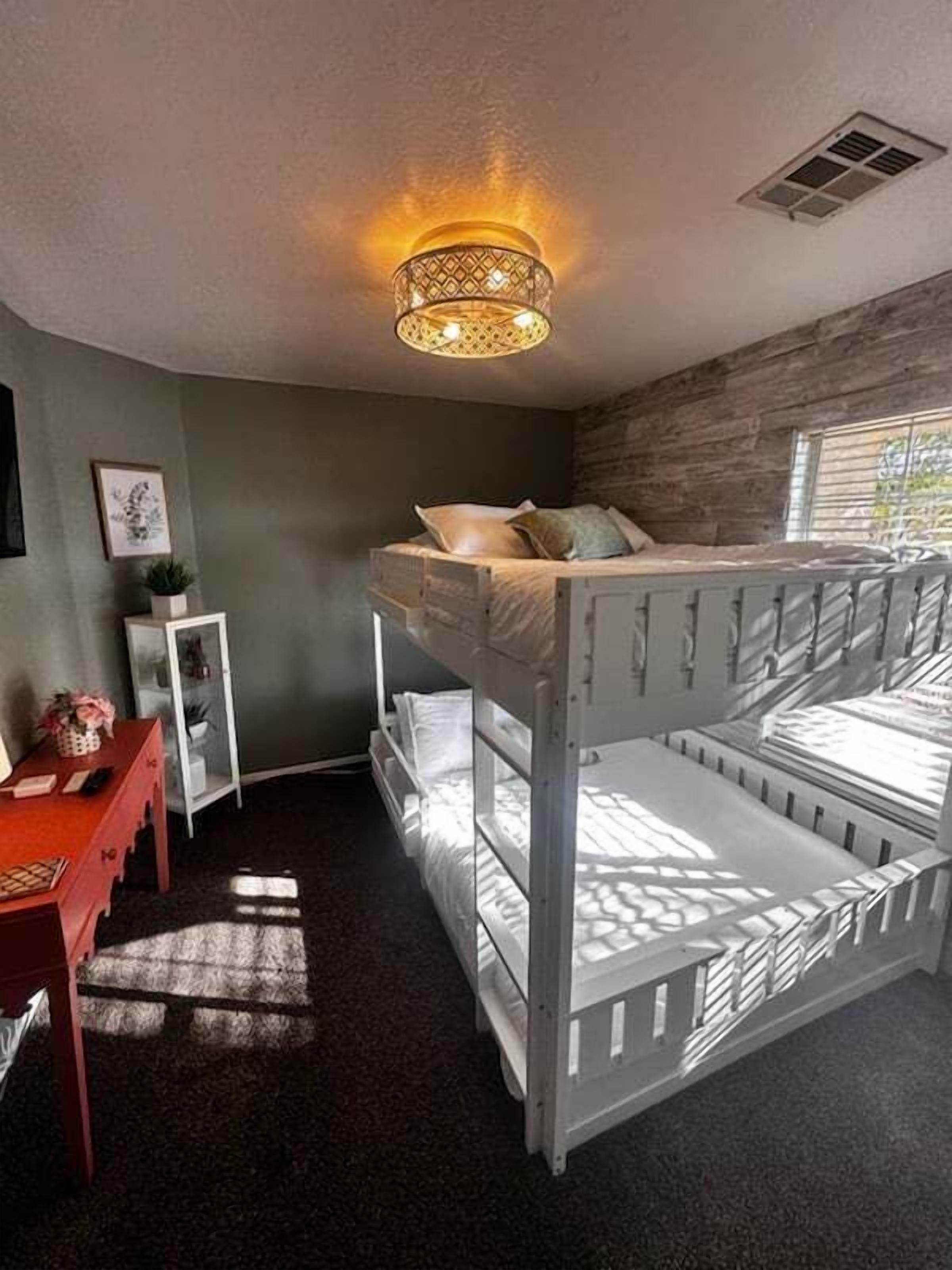 A bunk bed room with a ceiling light fixture, a desk, and a window.