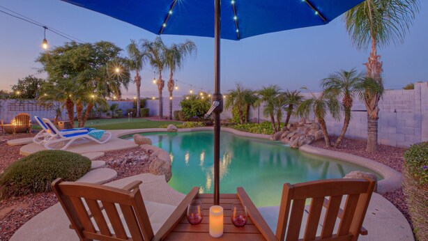 Zona de piscina con sillones de descanso, una mesa con velas y luces colgantes.