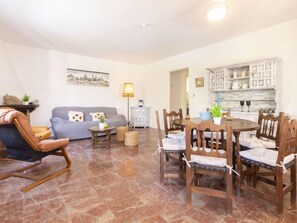 Een woonkamer met een bank, een houten schommelstoel, een eettafel met stoelen, een lamp en een decor kast.