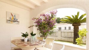A patio with a round table and chairs, surrounded by potted plants and a view of a white building and palm tree.