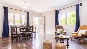A spacious living room with a dining area, large windows with blue curtains, and a ceiling fan.
