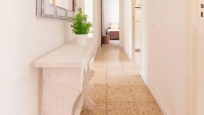 A narrow hallway with a white bench, a potted plant, and a bed visible in the distance.