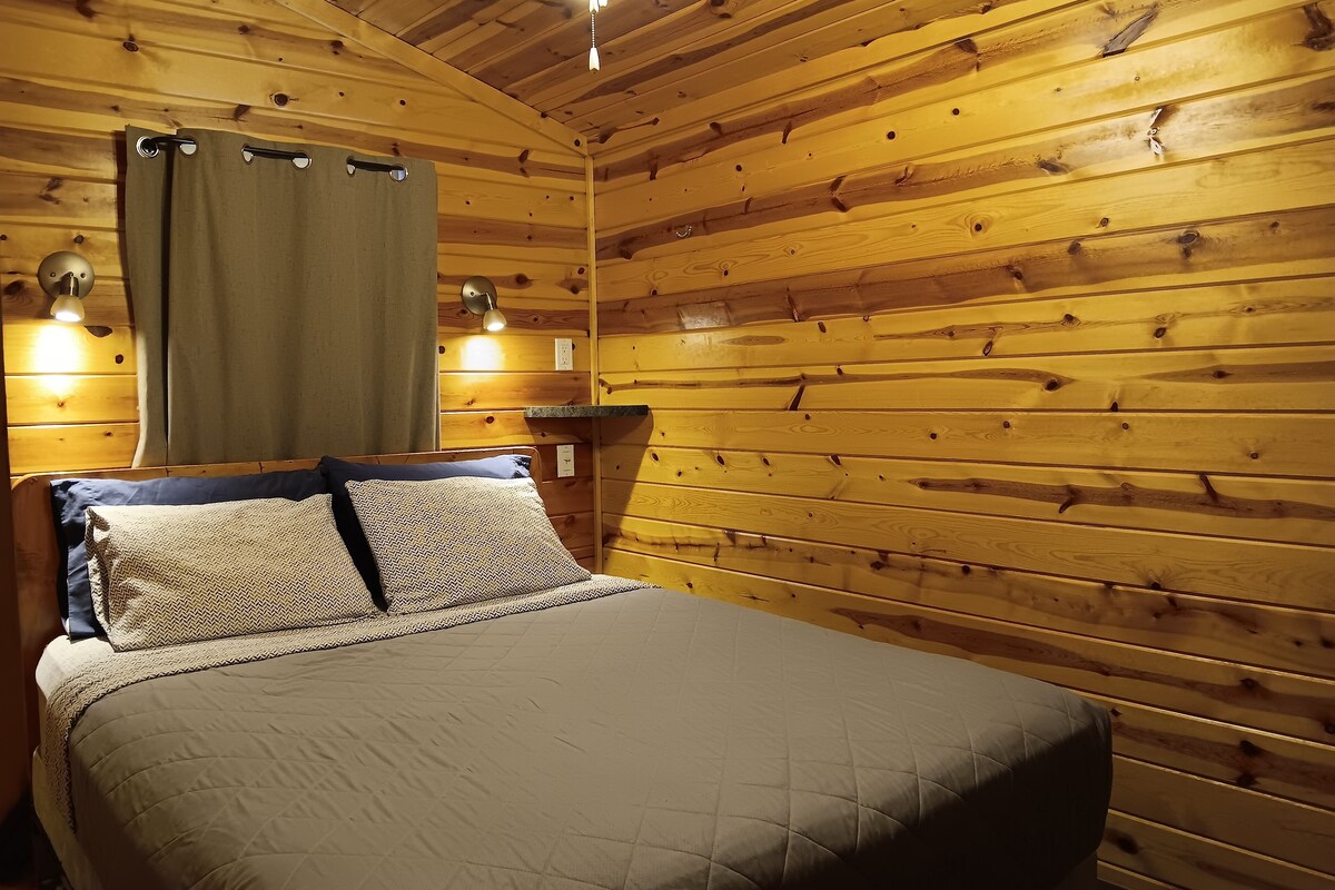 A wooden-paneled room with a bed, two wall-mounted lamps, and a ceiling light.