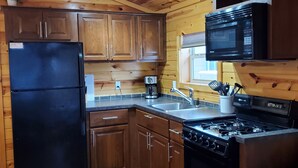A wooden-paneled kitchen with a black refrigerator, stove, and microwave.